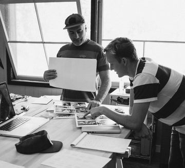 Two people working together at a desk with photos and a laptop.