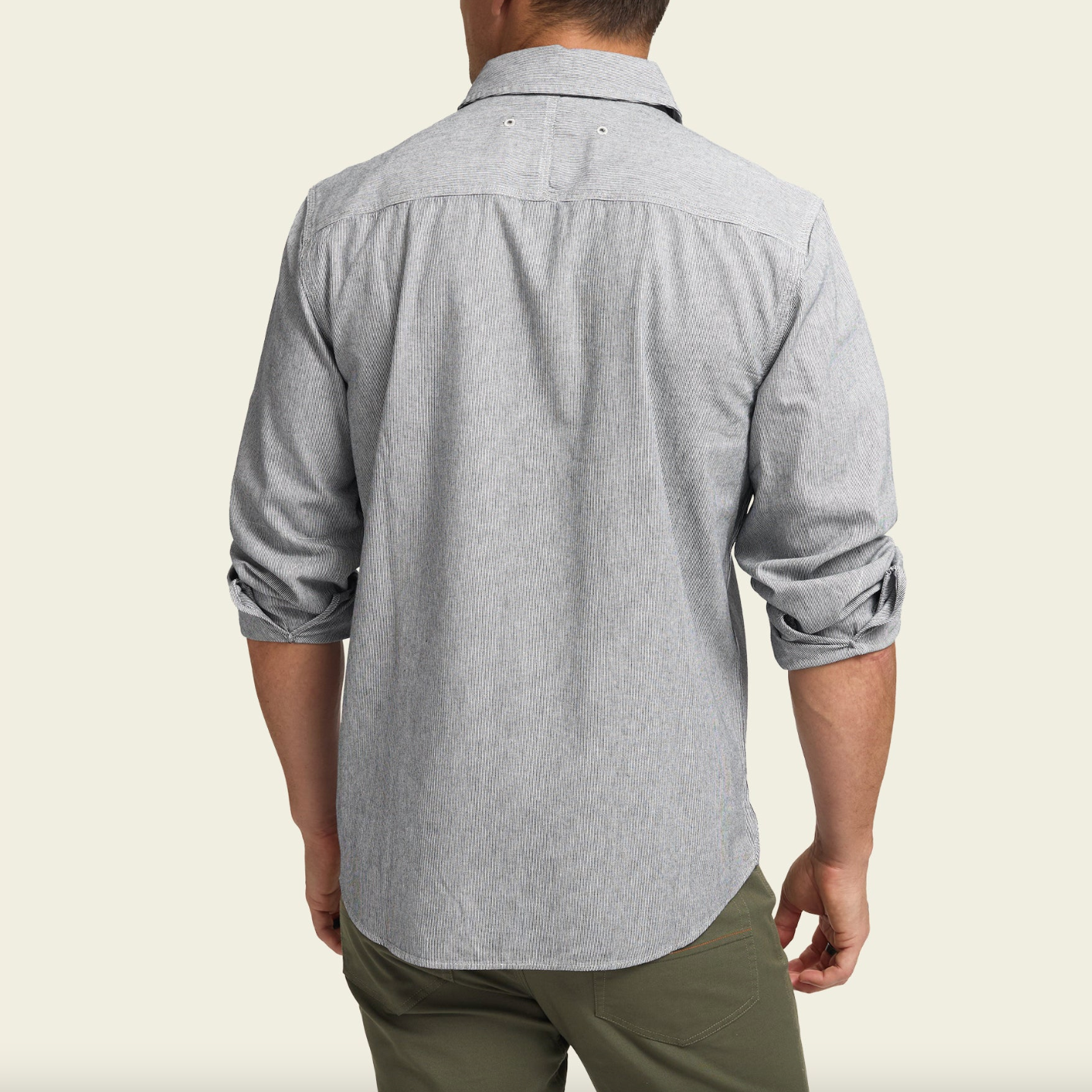 Person wearing a gray patterned shirt with rolled-up sleeves on a beige background